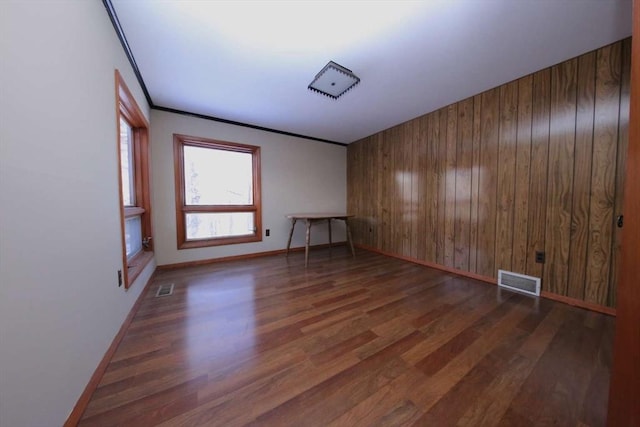 empty room with dark wood-type flooring, crown molding, and wood walls