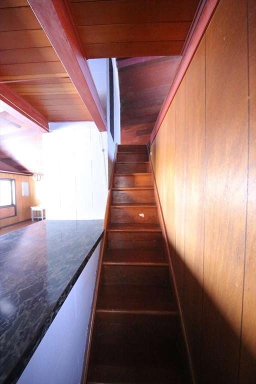 stairs featuring wood-type flooring, beamed ceiling, wooden walls, and wooden ceiling