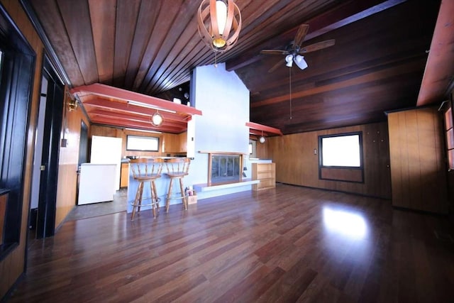 unfurnished living room with ceiling fan, lofted ceiling with beams, dark wood-type flooring, bar area, and wooden ceiling