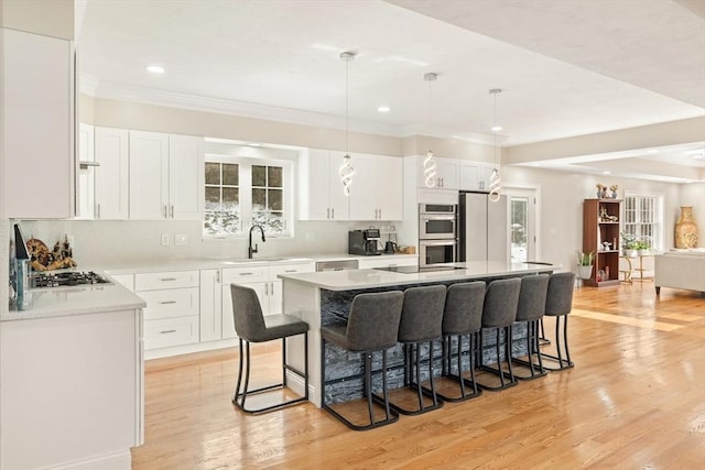 kitchen with sink, white cabinetry, pendant lighting, stainless steel appliances, and a kitchen island with sink