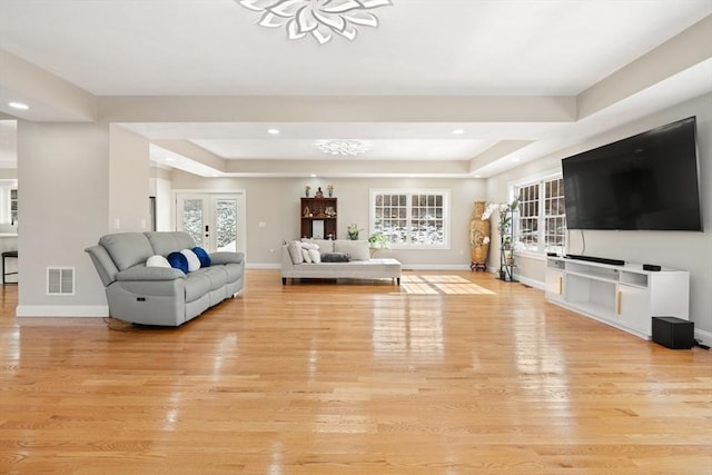 unfurnished living room featuring light hardwood / wood-style floors, french doors, and a raised ceiling