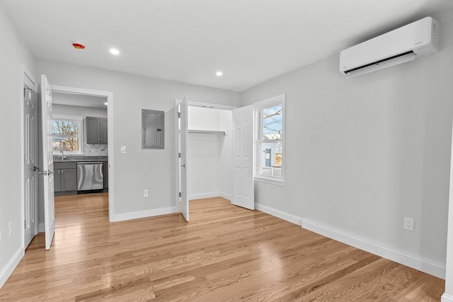 unfurnished bedroom featuring light hardwood / wood-style flooring, an AC wall unit, multiple windows, and electric panel