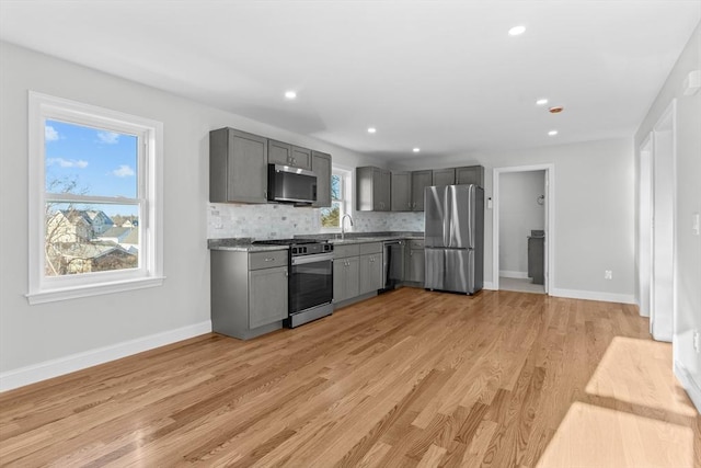 kitchen with decorative backsplash, sink, light hardwood / wood-style flooring, gray cabinetry, and stainless steel appliances