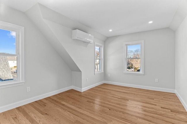 additional living space featuring lofted ceiling, light hardwood / wood-style flooring, and a wall unit AC