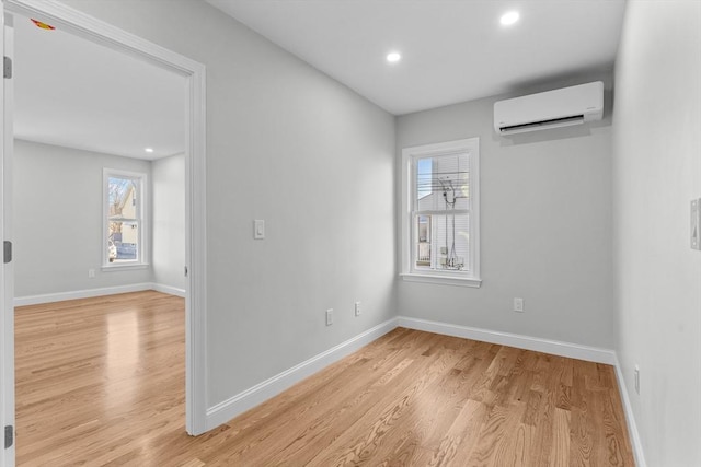 unfurnished room with an AC wall unit, plenty of natural light, and light hardwood / wood-style flooring