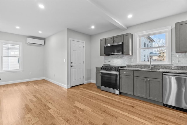 kitchen with gray cabinets, a wall unit AC, stainless steel appliances, light wood-type flooring, and sink