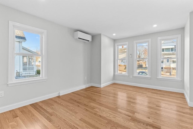 unfurnished room with light wood-type flooring, a wall mounted AC, and a wealth of natural light