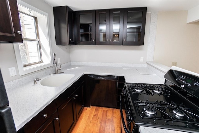 kitchen with black appliances, a sink, light wood finished floors, glass insert cabinets, and light countertops