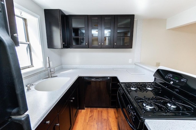 kitchen with glass insert cabinets, light countertops, light wood-style floors, black appliances, and a sink