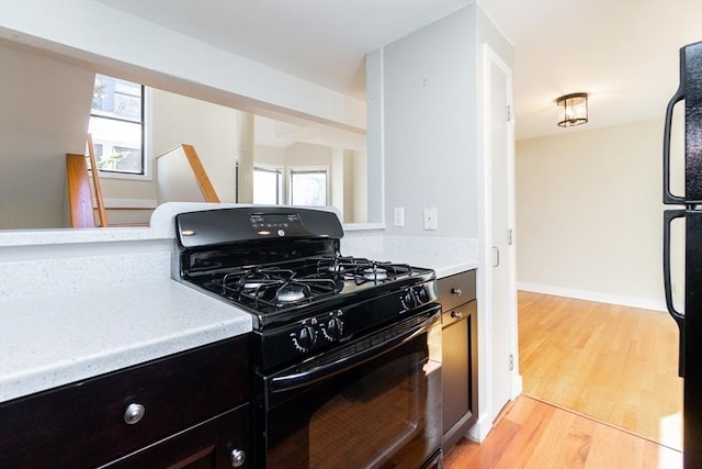 kitchen with light wood-type flooring, black appliances, and light countertops