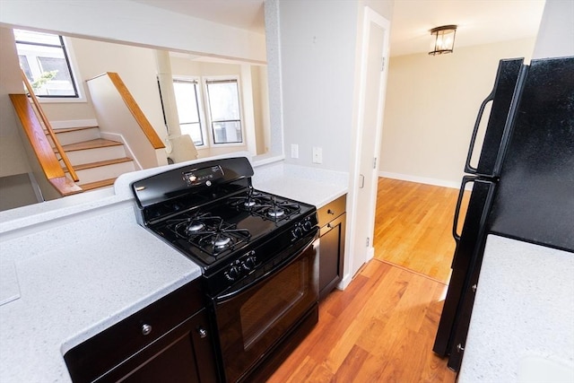 kitchen featuring light wood finished floors, black appliances, light countertops, and baseboards