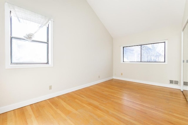 empty room featuring lofted ceiling, light wood-style floors, baseboards, and visible vents