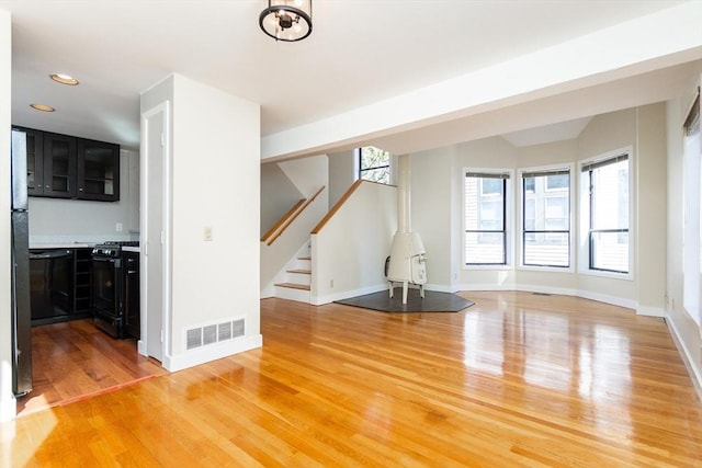 unfurnished living room featuring light wood-type flooring, visible vents, baseboards, and stairs