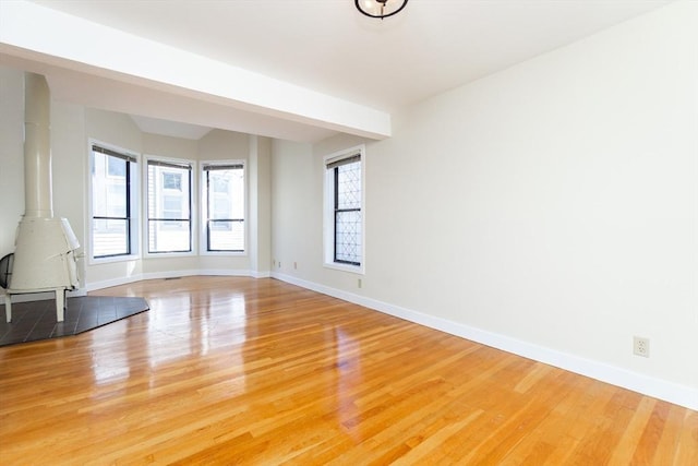 unfurnished living room with light wood-style flooring, a wood stove, and baseboards