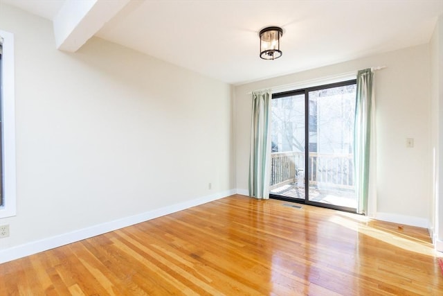 empty room with beam ceiling, visible vents, baseboards, and wood finished floors