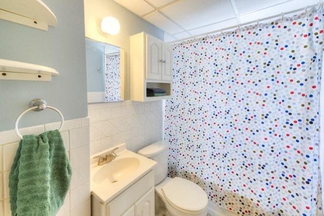 full bathroom featuring toilet, shower / tub combo, tile walls, vanity, and a drop ceiling