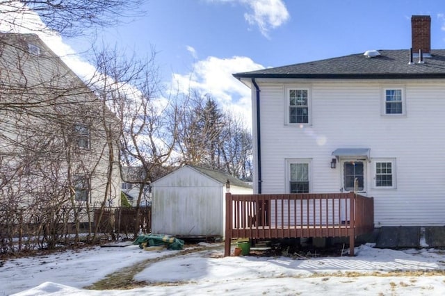 snow covered house featuring a wooden deck and a storage shed