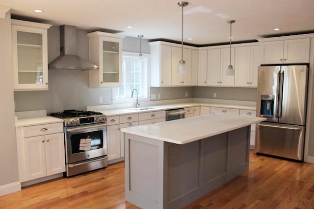 kitchen featuring light wood finished floors, a sink, wall chimney range hood, light countertops, and appliances with stainless steel finishes