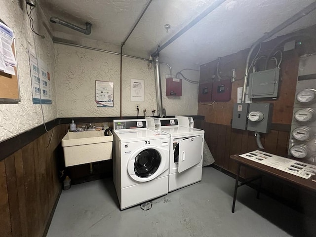 shared laundry area featuring electric panel, a textured wall, wood walls, separate washer and dryer, and a sink