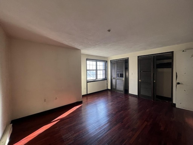 unfurnished bedroom featuring wood finished floors, two closets, and baseboards