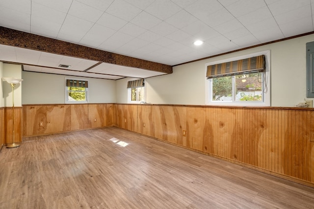 basement with wooden walls, light hardwood / wood-style flooring, ornamental molding, and a wealth of natural light