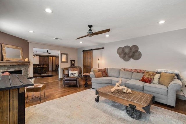 living room with ceiling fan, a barn door, a fireplace, and wood finished floors