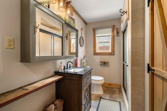 bathroom featuring toilet, a shower with shower door, baseboards, and vanity