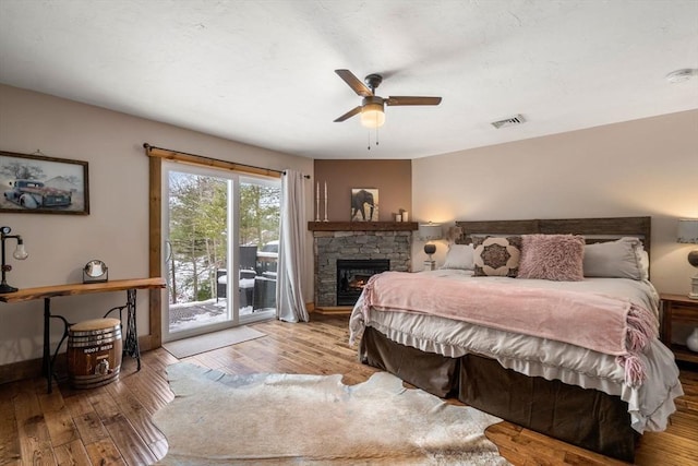 bedroom featuring baseboards, visible vents, hardwood / wood-style floors, access to exterior, and a stone fireplace