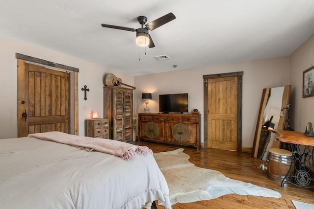 bedroom featuring a ceiling fan, visible vents, and wood finished floors