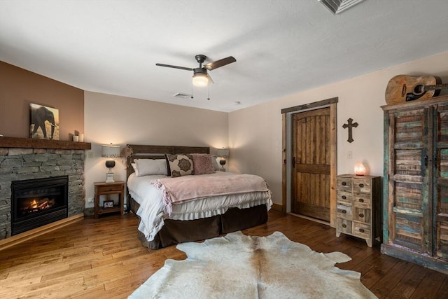 bedroom featuring a stone fireplace, visible vents, baseboards, a ceiling fan, and wood-type flooring