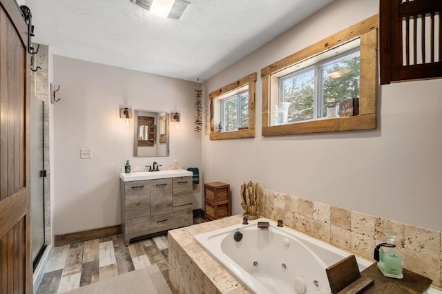 bathroom featuring a textured ceiling, wood finished floors, vanity, baseboards, and a jetted tub