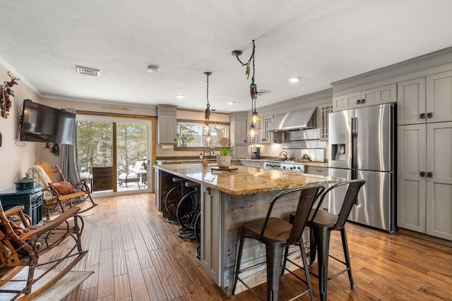 kitchen featuring a kitchen breakfast bar, stainless steel refrigerator with ice dispenser, gray cabinetry, and wall chimney range hood