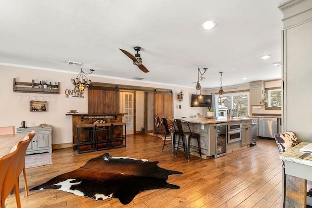 living area with light wood-type flooring, a barn door, visible vents, and ceiling fan