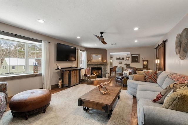 living room featuring ceiling fan, a stone fireplace, a barn door, and wood finished floors