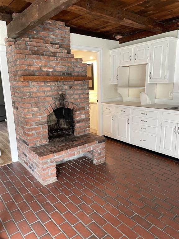 kitchen featuring white cabinets, wooden ceiling, beam ceiling, and brick floor