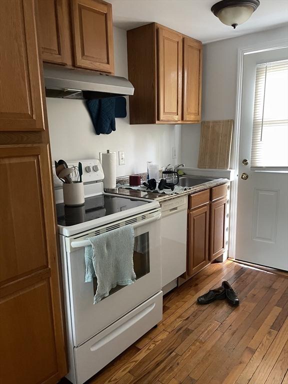 kitchen with hardwood / wood-style floors, white appliances, under cabinet range hood, brown cabinets, and a sink
