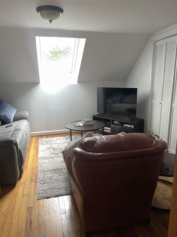 living area with baseboards, lofted ceiling with skylight, and hardwood / wood-style flooring