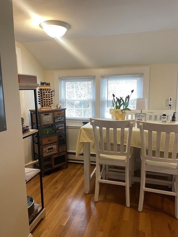 dining area with a baseboard heating unit, wood finished floors, and lofted ceiling