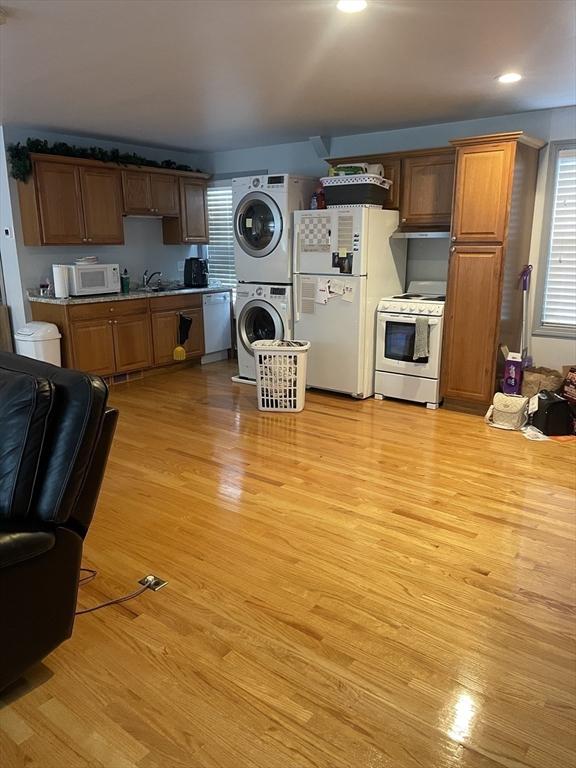 kitchen featuring a sink, light wood-style flooring, stacked washer and dryer, and white appliances