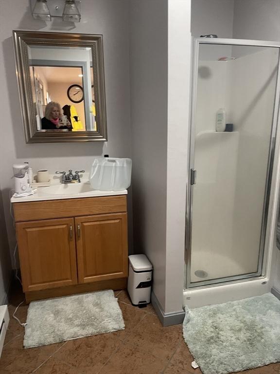 full bath featuring tile patterned flooring, vanity, baseboards, a shower stall, and a baseboard radiator