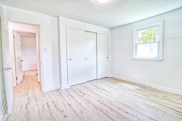 unfurnished bedroom featuring light wood-style flooring, a closet, and baseboards