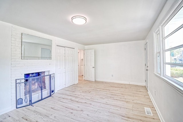 unfurnished living room featuring light wood-type flooring, baseboards, and a brick fireplace