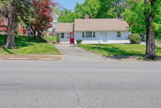 view of front of house featuring asphalt driveway, a chimney, and a front lawn