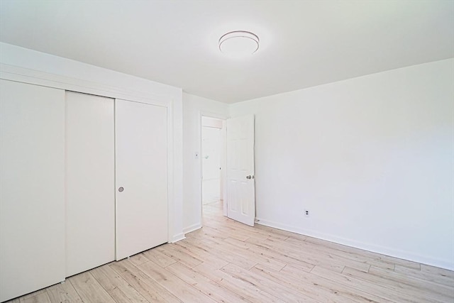 unfurnished bedroom featuring light wood-style floors, a closet, and baseboards