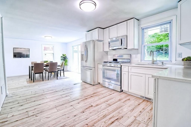 kitchen with appliances with stainless steel finishes, a sink, light wood finished floors, and light countertops