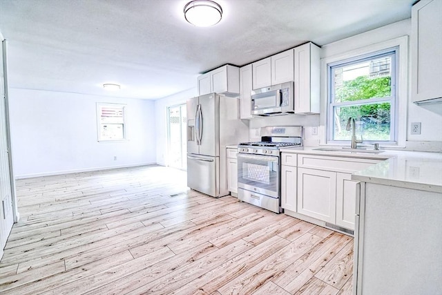 kitchen with stainless steel appliances, light wood-style flooring, a sink, and light countertops