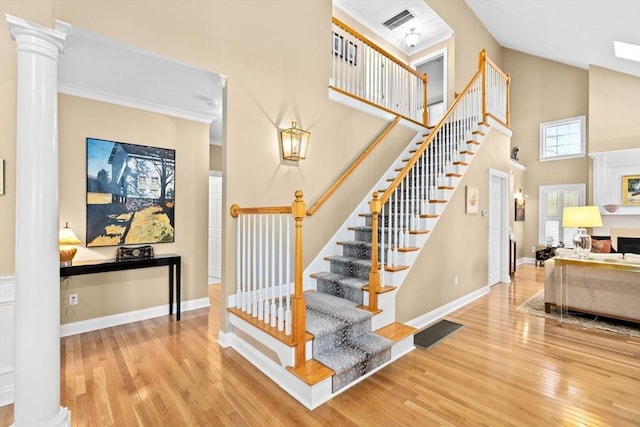 stairs featuring decorative columns, hardwood / wood-style floors, a high ceiling, and ornamental molding