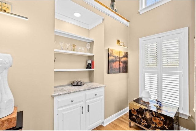 bar with white cabinetry, light stone countertops, built in features, light hardwood / wood-style flooring, and ornamental molding