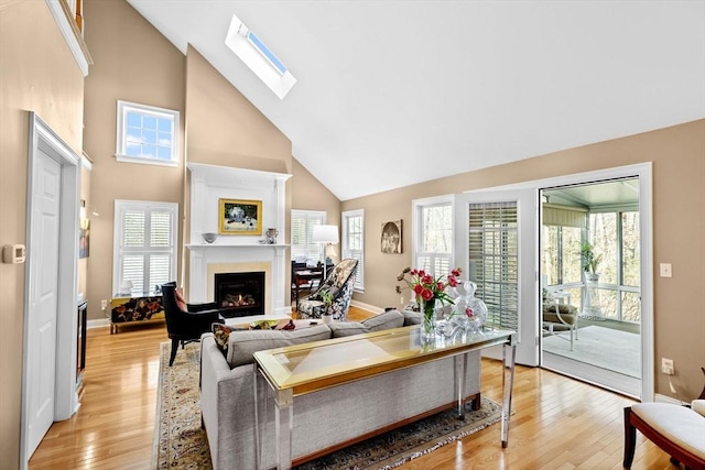 living room with a skylight, high vaulted ceiling, and light hardwood / wood-style flooring