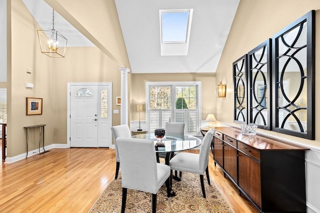 dining space with a skylight, a chandelier, a towering ceiling, light hardwood / wood-style floors, and decorative columns